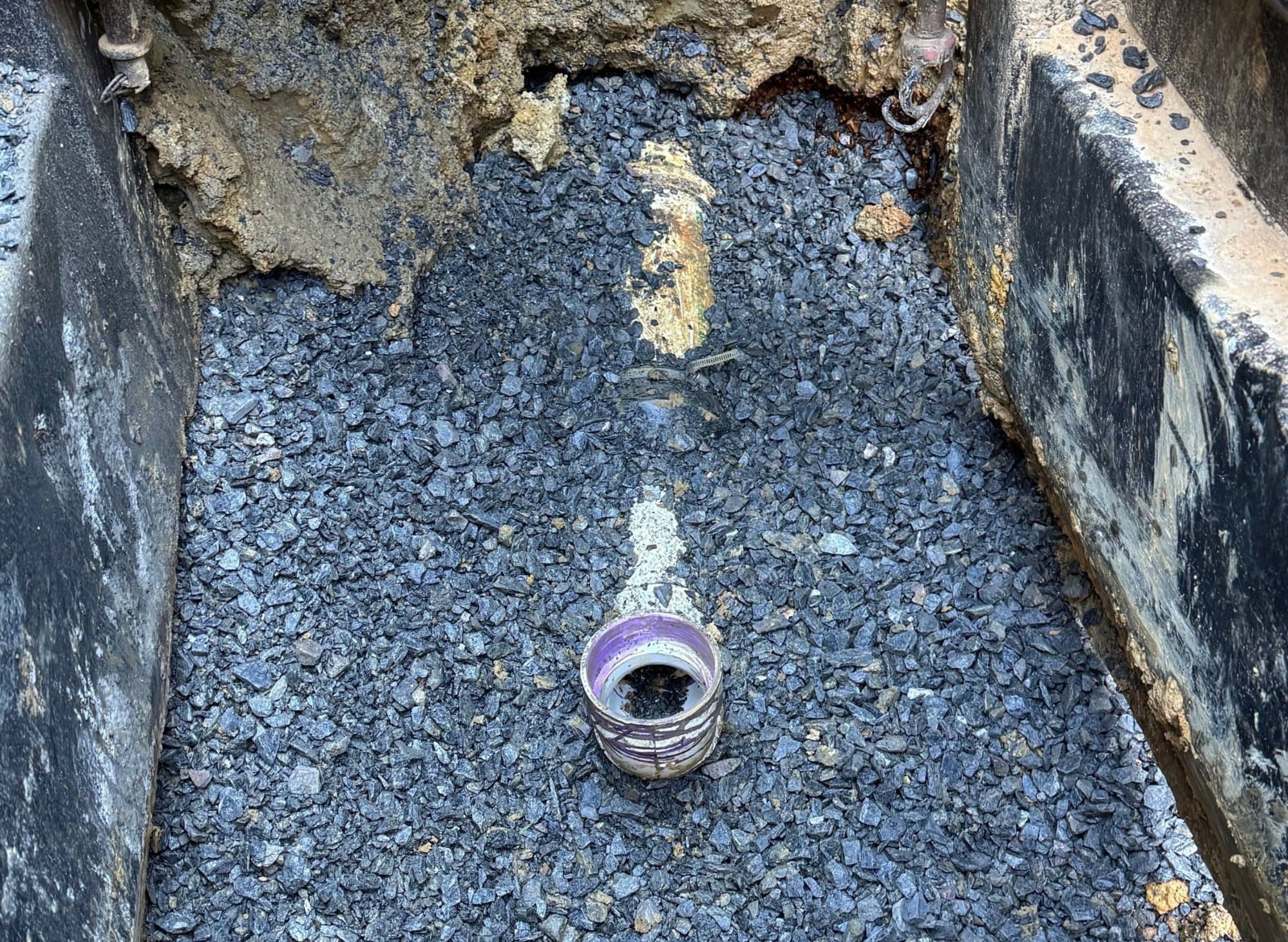 New PVC sewer cleanout riser set in crushed stone bedding at the bottom of a shored trench